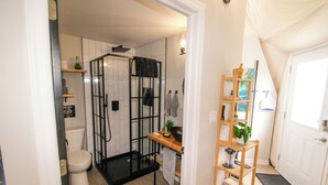 A bathroom with a glass shower enclosure, a toilet, and a wooden shelf with a plant.