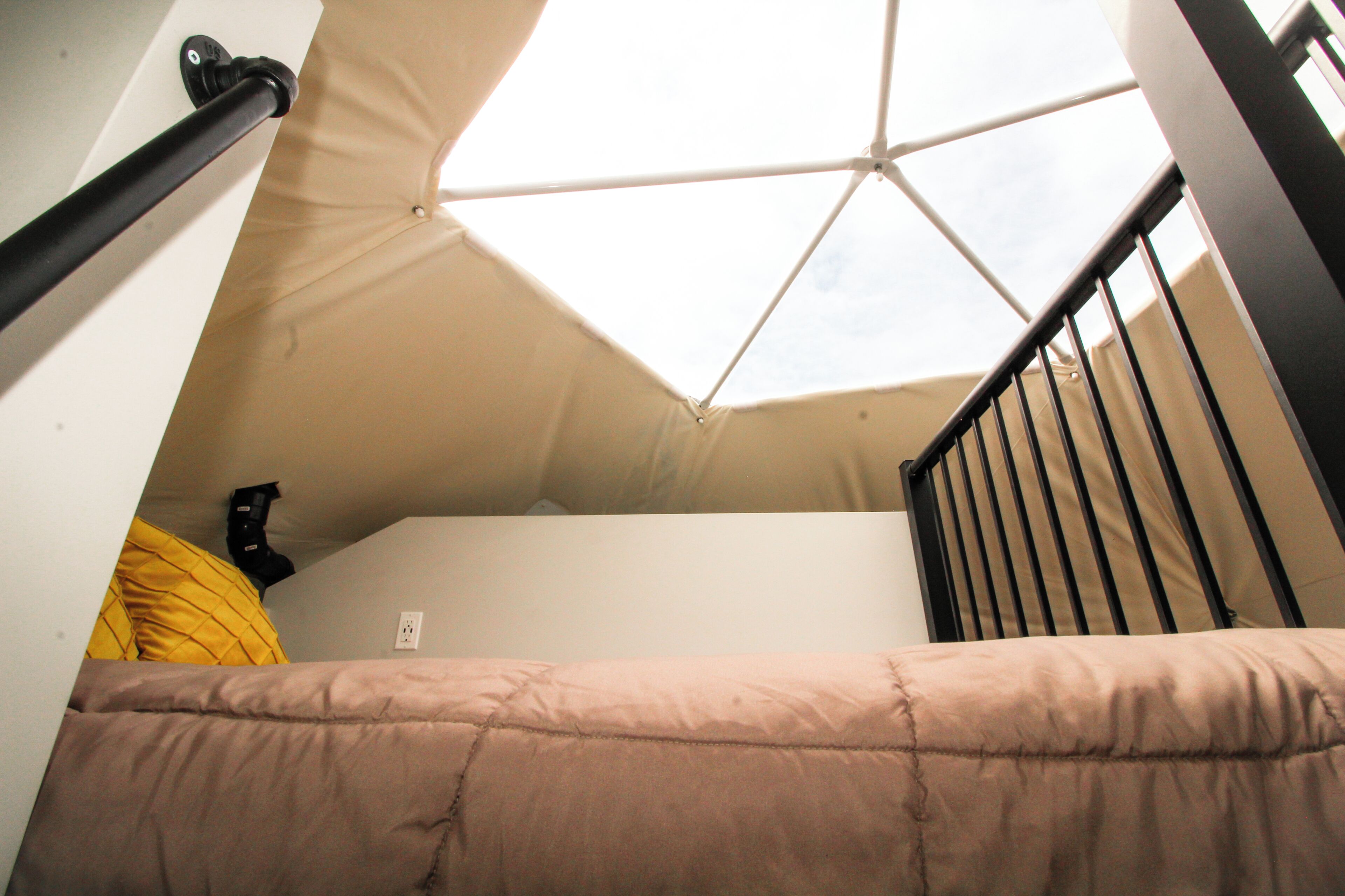 A dorm-style room with a bunk bed, a skylight, and a black railing.