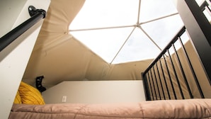 A dorm-style room with a bunk bed, a skylight, and a black railing.