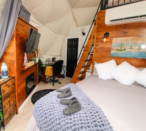 A cozy tent-style room with a bed, a desk, a chair, and a ladder.