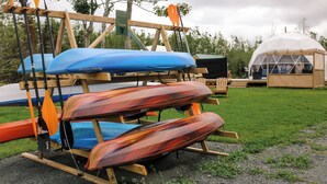 A row of canoes and paddles on a wooden rack, a tent in the background, and a grassy area. - Nautical Dome Accommodations (Monks Head)