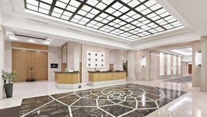 Un hall d’hôtel comprenant un comptoir d’accueil, un sol orné de motifs géométriques et un plafond en lucarne.