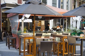 An outdoor café with tables and chairs, a bar area, and a person working behind the counter.