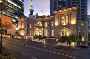A historic building with classical architecture, a prominent entrance, and a view of a modern skyscraper in the background. - Level 25 1 Bed with Marble Lined Bath City Views (Auckland)