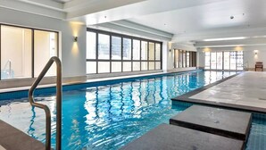 An indoor swimming pool with clear blue water, surrounded by large windows and a bench. - Level 25 1 Bed with Marble Lined Bath City Views (Auckland)