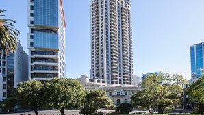 A tall, modern high-rise building with multiple balconies, surrounded by trees and other buildings. - Level 25 1 Bed with Marble Lined Bath City Views (Auckland)