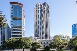 Un grand immeuble moderne, doté de nombreux balcons, entouré d’arbres et d’autres bâtiments.
