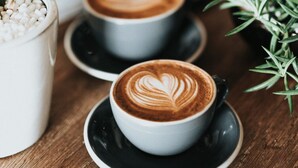 Two cups of coffee with latte art on a wooden table, accompanied by a potted plant and a white container with white beads. - Hobson Quay Penthouse 3 Bed Views Parking Viaduct (Auckland)
