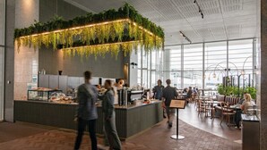 A modern restaurant with a central counter, seating area, and large windows.