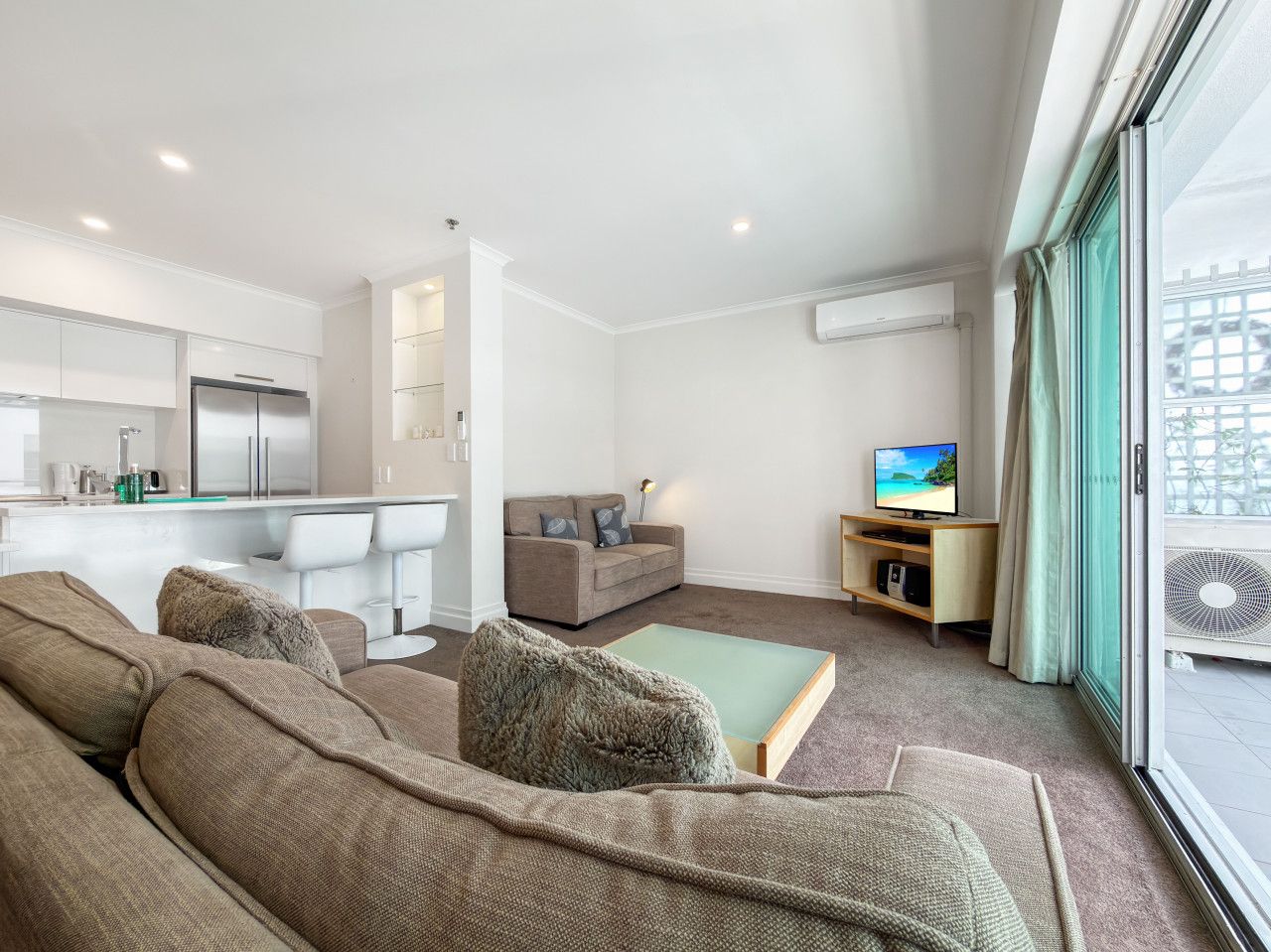 Ein modernes Wohnzimmer mit einer Couch, einem Couchtisch, einem Fernseher und einem Balkon mit Blick.