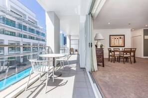 A balcony with a pool, a dining area with chairs, and a view of a cruise ship.