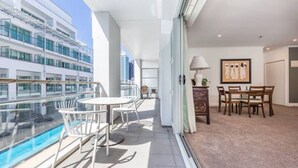 A balcony with a pool, a dining area with chairs, and a view of a cruise ship.