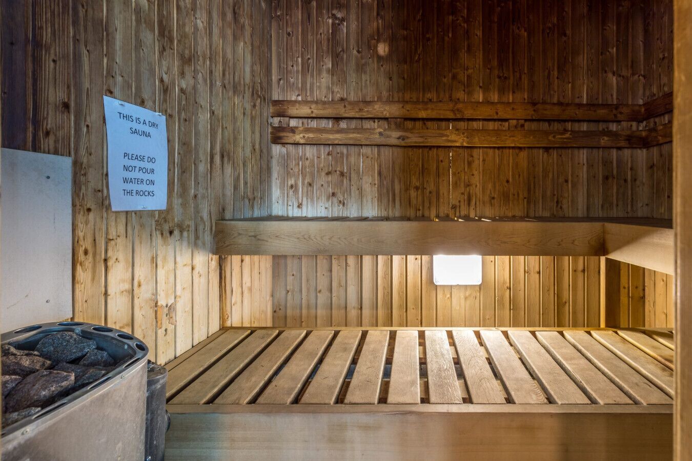 Eine Trocken-Sauna mit Holzbänken und einem Schild, das darauf hinweist, kein Wasser auf die Steine zu schütten.