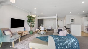 A modern living room with a flat-screen TV, a large potted plant, a dining area with a table and chairs, and a kitchen area with a bar counter. - Gorgeous Waterfront Apartment Harbour and Views (Auckland)
