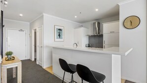 A modern kitchen with white cabinetry, a stainless steel range hood, and a small island with two black bar stools. - Gorgeous Waterfront Apartment Harbour and Views (Auckland)