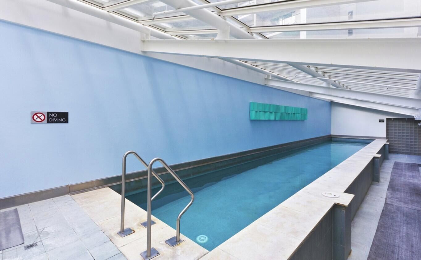 An indoor swimming pool with a no diving sign, a tiled floor, and a glass ceiling.