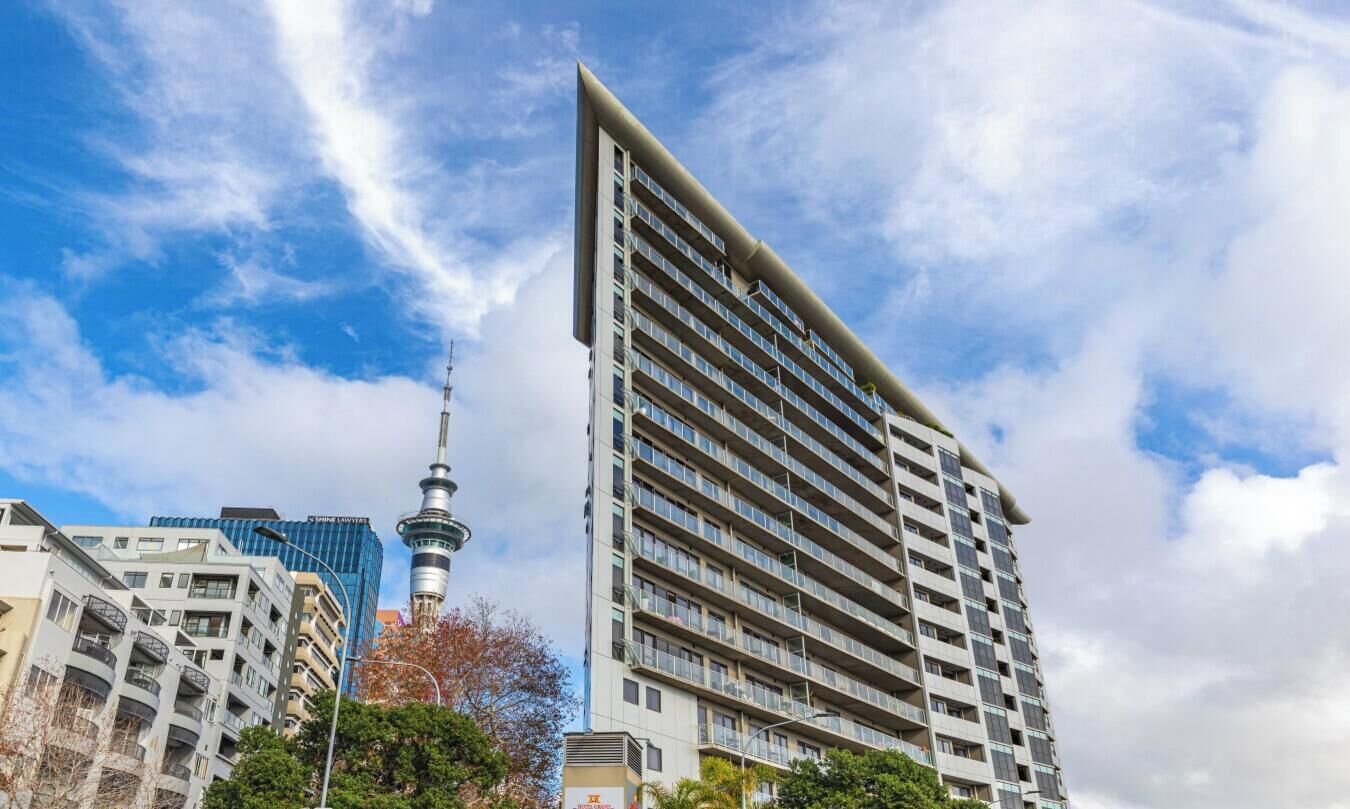 A high-rise building with a modern design, featuring multiple balconies and a prominent tower in the background.