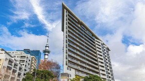 Ein Hochhaus mit modernem Design, das mehrere Balkone und einen markanten Turm im Hintergrund zeigt.