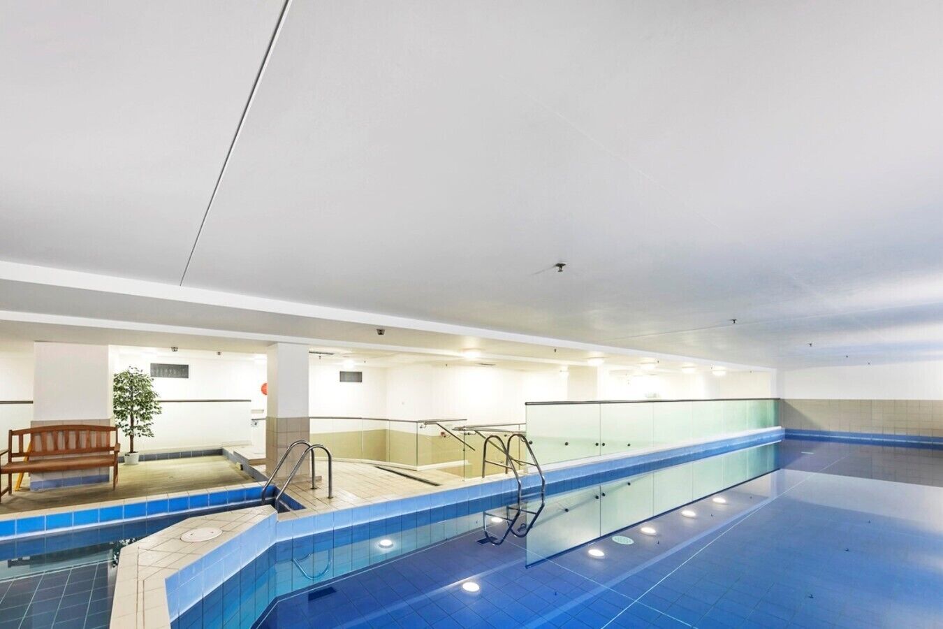Piscina com área de vestiários, um banco e uma planta.