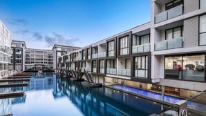 A modern hotel with a swimming pool, multiple balconies, and a clear sky.