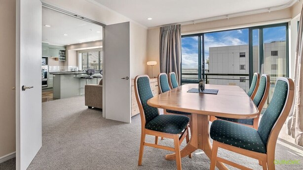 Une chambre d’hôtel dotée d’un coin repas comprenant une table en bois et des chaises recouvertes d’un tissu vert, une grande fenêtre avec des rideaux et une vue sur le paysage urbain.