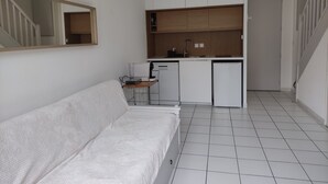 A compact kitchenette with a small fridge, sink, and wooden cabinets.
