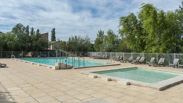 A rooftop swimming pool with two separate sections, surrounded by lounge chairs and a fence.
