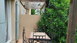 A covered patio with a table and chairs, surrounded by greenery and a tiled floor.