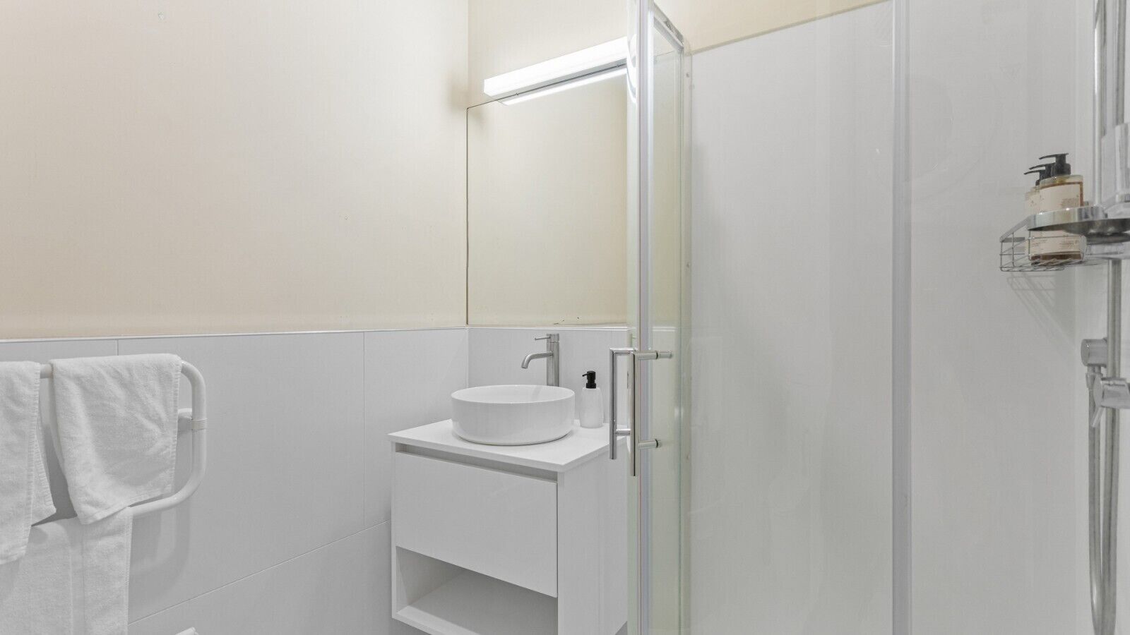 Une salle de bain avec une douche à parois de verre, un lavabo blanc doté d’un distributeur de savon et un porte-serviettes.