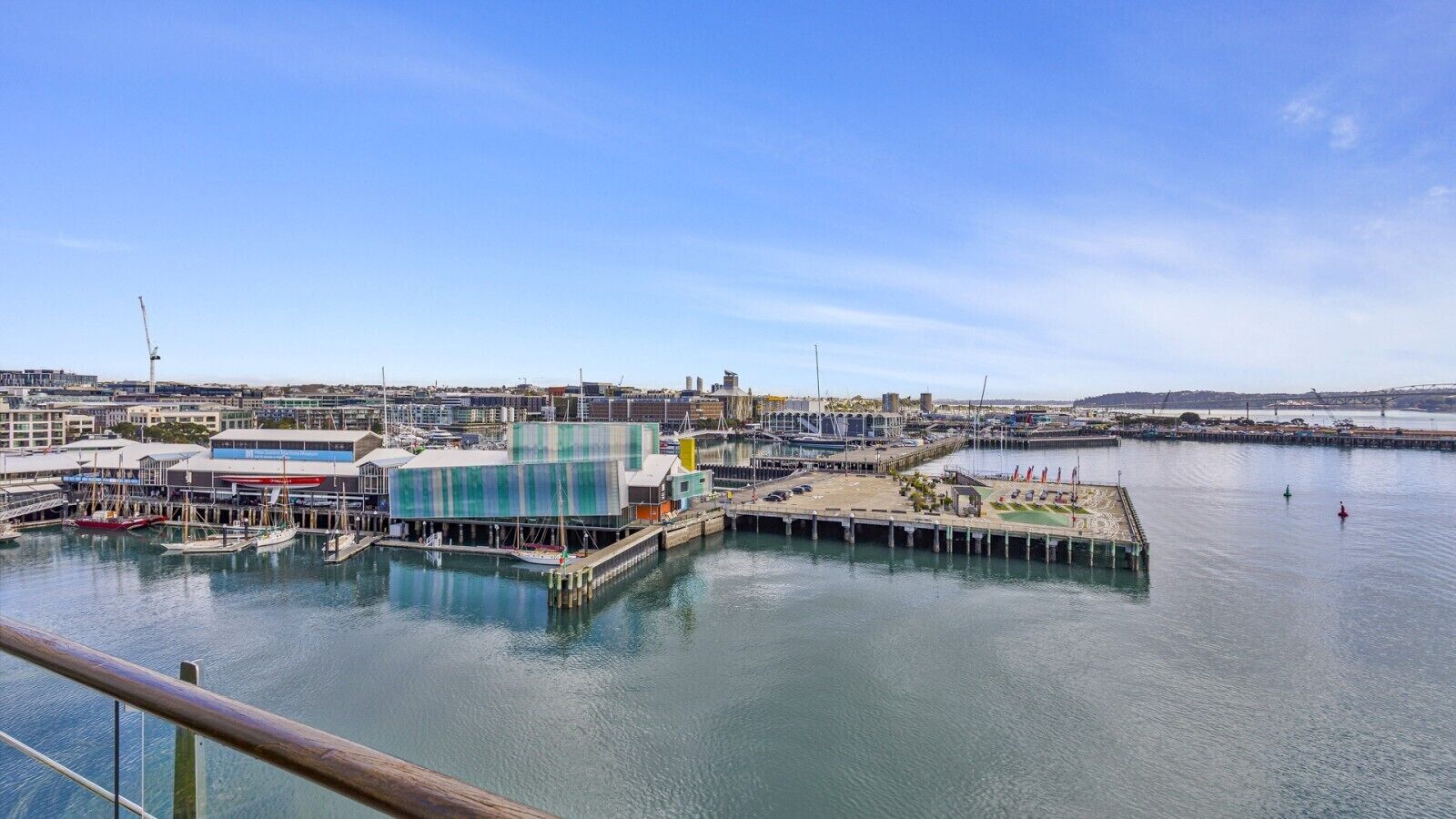 A marina with boats docked, a building with a green facade, and a clear sky.