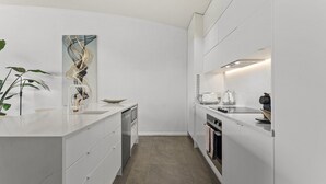 Cocina moderna con armarios blancos, lavavajillas, horno y pileta. Hay una planta a la izquierda y un cuadro en la pared.