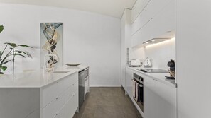 A modern kitchen with white cabinetry, a dishwasher, an oven, and a countertop with a coffee maker and a kettle. - Spacious 3-Bed Waterfront Apartment (Auckland)