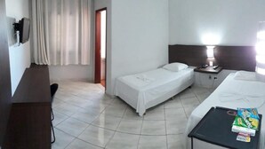 A hotel room with two beds, a desk, a chair, a TV, and a nightstand with a lamp. - Bravo City Hotel Primavera do Leste (Primavera do Leste)