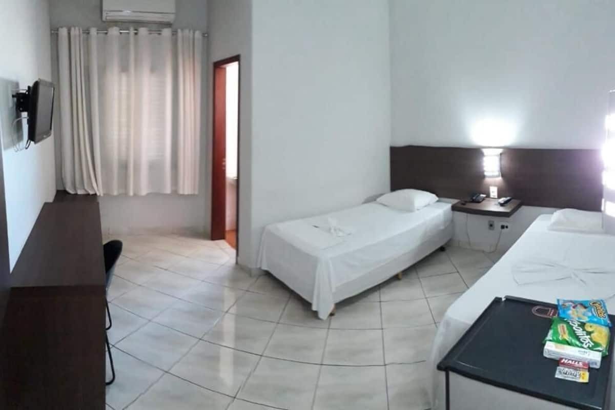 Habitación de hotel con dos camas, un escritorio, una silla, un televisor y una mesita de noche con lámpara.