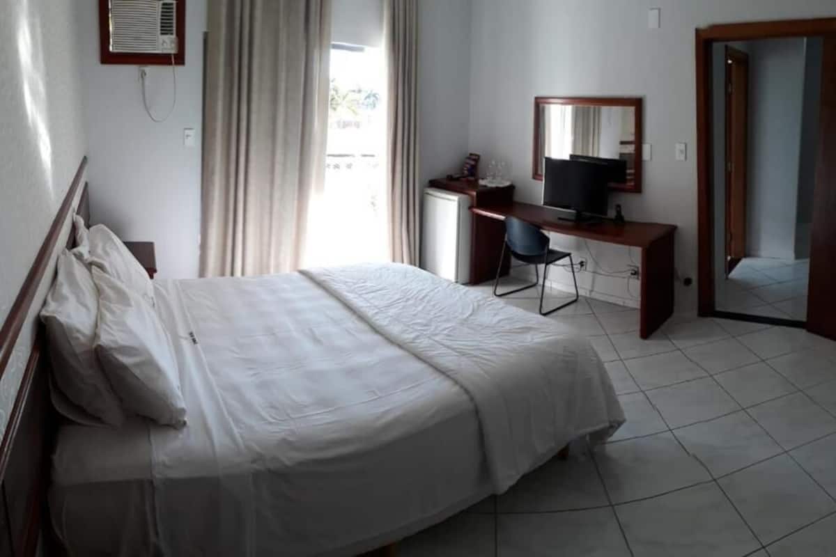 Una habitación de hotel con cama, escritorio con silla, televisor y espejo.