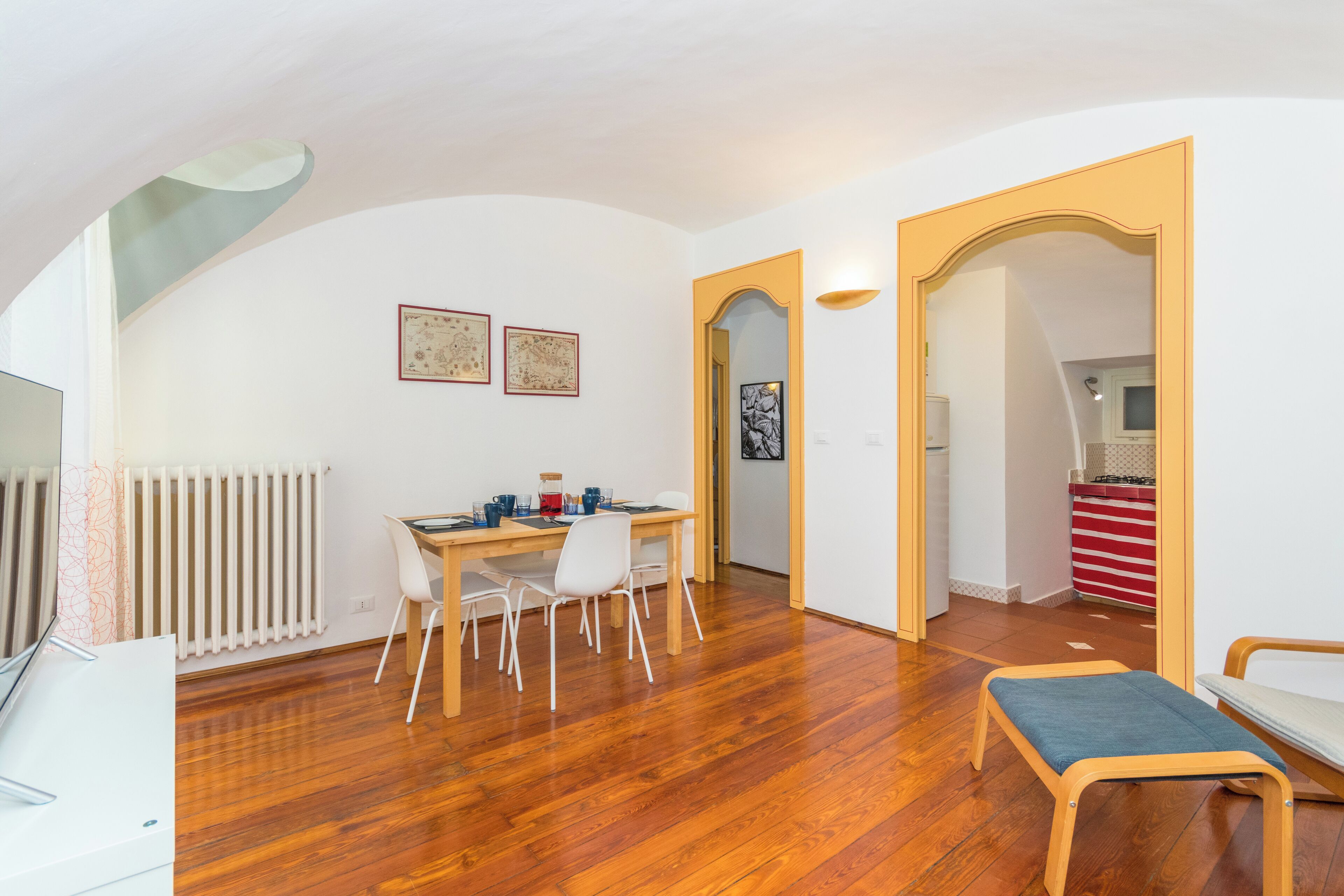 A modern apartment with a dining area, a small seating area, and a kitchen visible through an archway.