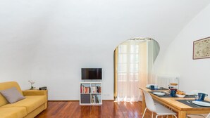 Ein gemütliches Wohnzimmer mit einer Couch, einem Fernseher, einem Bücherregal und einem Essbereich mit Tisch und Stühlen.