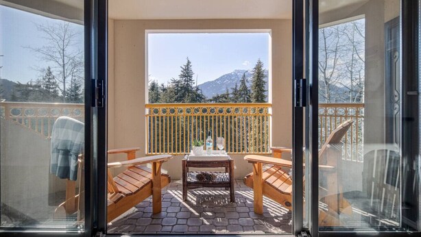A balcony with a table and chairs, a view of trees and mountains, and a railing. - The Mountain View Condo - Large 2BR/2BA (Whistler)