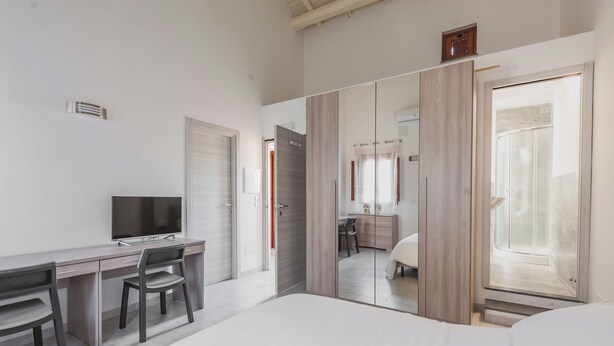 Una habitación de hotel moderna con una cama, un escritorio con una silla, un televisor y una puerta corredera que da a un baño.