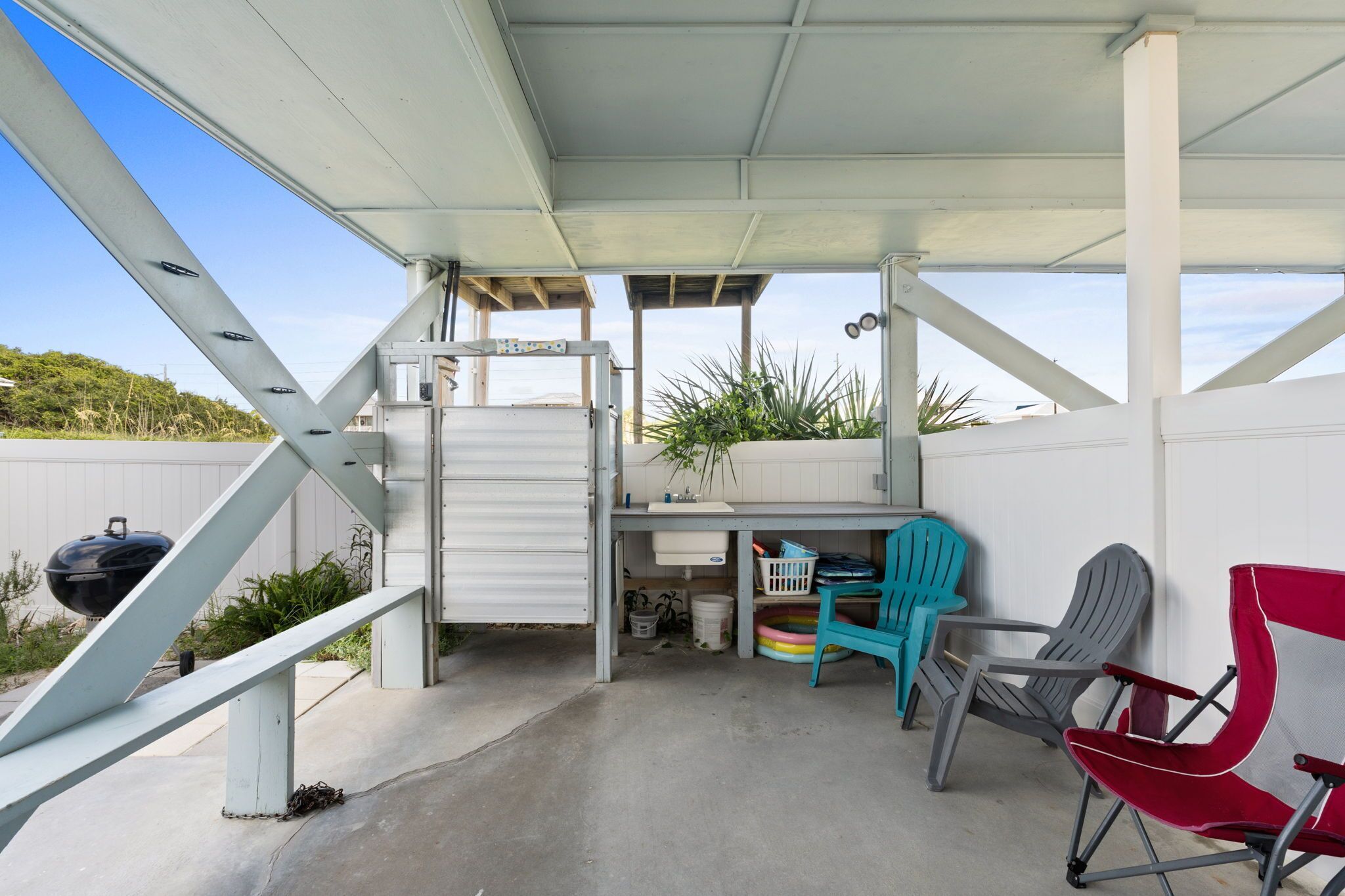 A covered outdoor patio with a concrete floor, a white metal structure, and a small table with a potted plant.