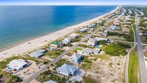 An aerial view of a coastal residential area with houses, a beach, and a road. - The Extra Mile, One Level, 2BR, Great for couples or small families! (Saint George Island)