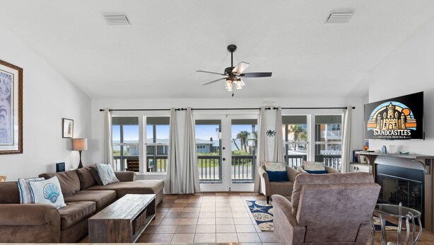 A spacious living room with a large sofa, a coffee table, and a fireplace. There is a television mounted on the wall and a ceiling fan above. - The Extra Mile, One Level, 2BR, Great for couples or small families! (Saint George Island)