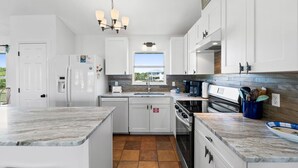 A modern kitchen with white cabinets, a marble countertop, a built-in oven, and a window providing a view of the outdoors. - The Extra Mile, One Level, 2BR, Great for couples or small families! (Saint George Island)