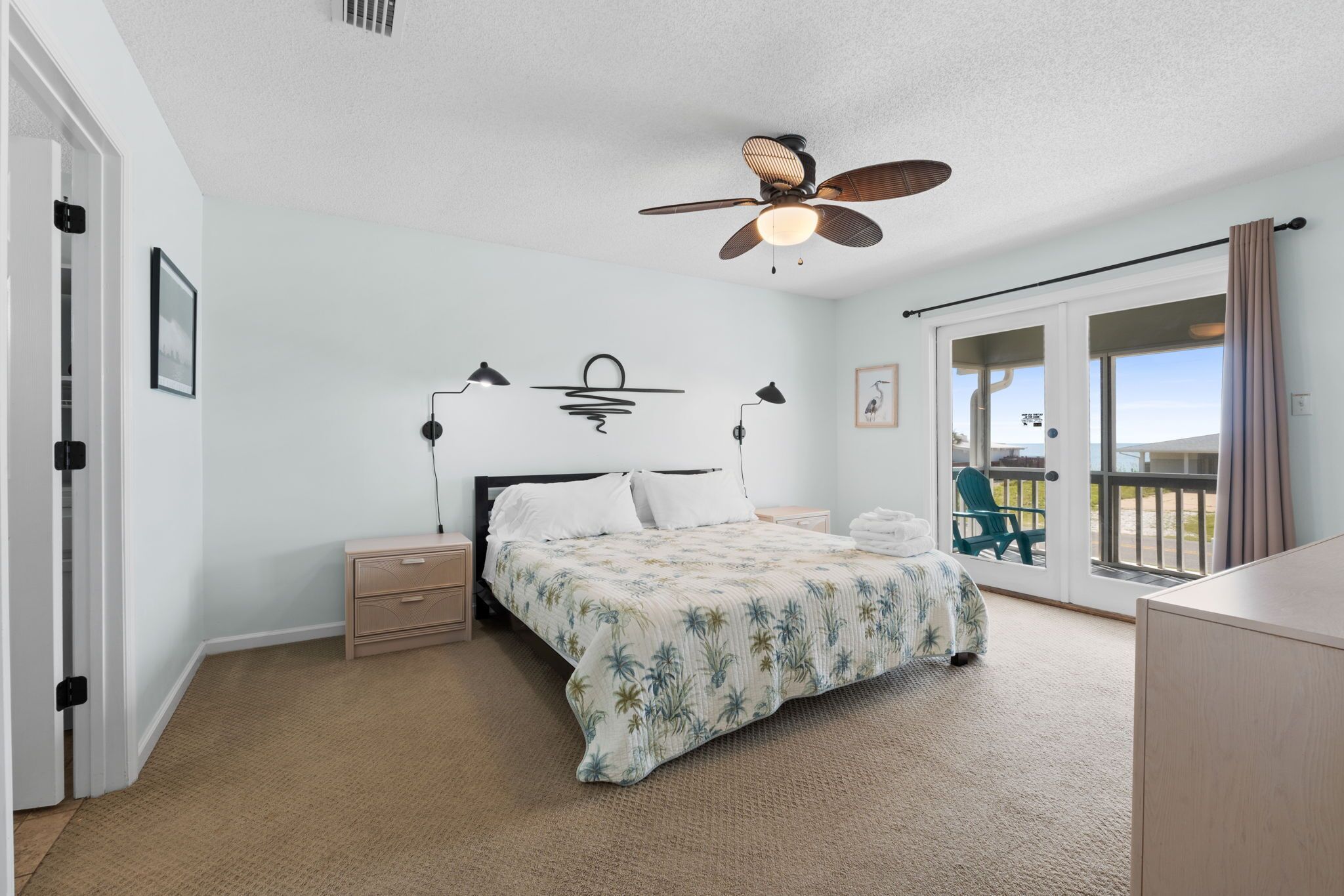 A bedroom with a bed, bedside tables, a ceiling fan, and a sliding glass door to a balcony.