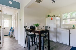 Une cuisine compacte comprenant une table à manger, deux chaises, un réfrigérateur et une fenêtre avec des stores.