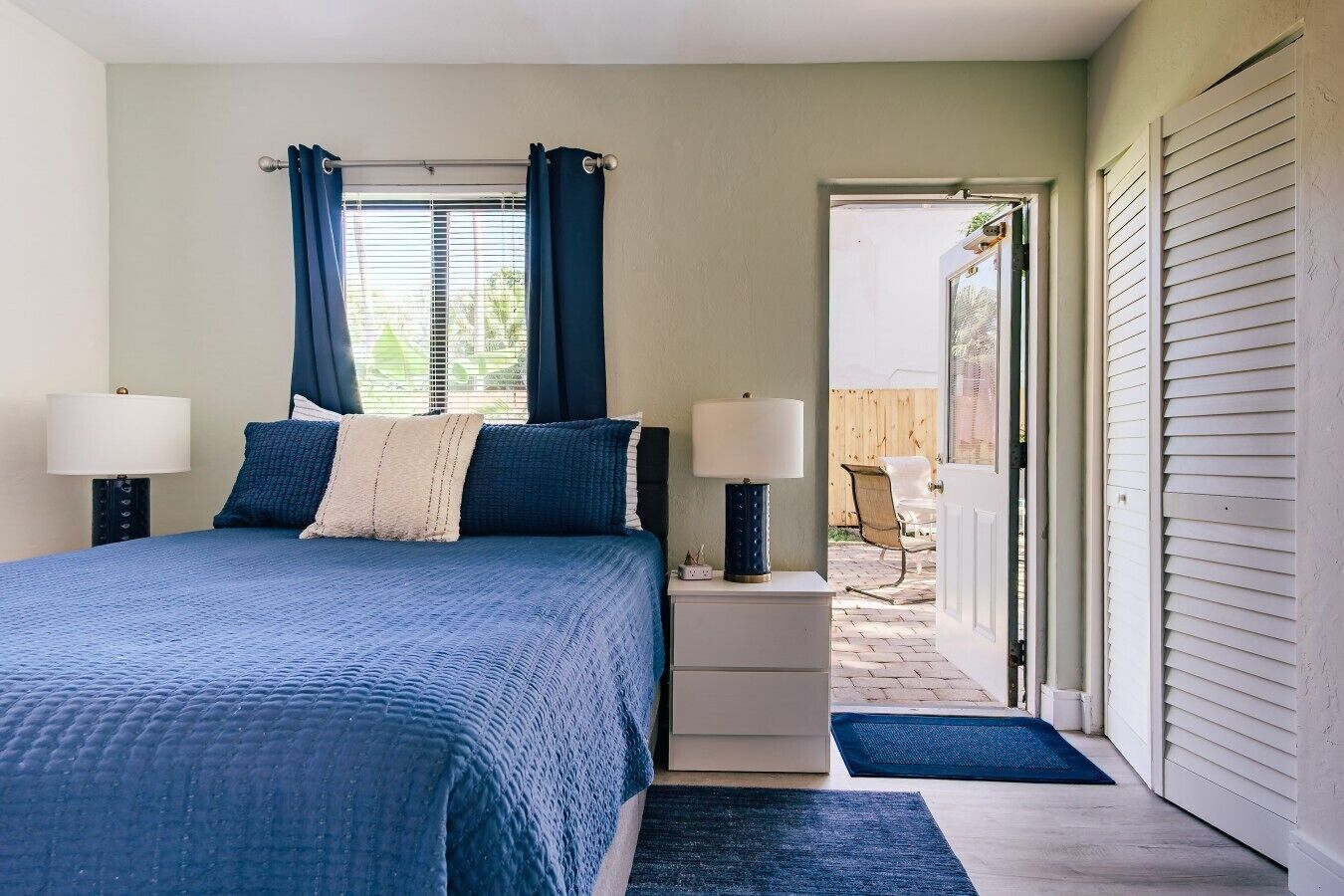 Une chambre à coucher avec un lit, deux tables de chevet avec des lampes, une fenêtre avec des rideaux et une vue sur l’extérieur.