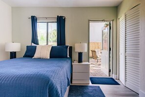 Un dormitorio con cama, dos mesitas de noche con lámparas, una ventana con cortinas y vistas al exterior.