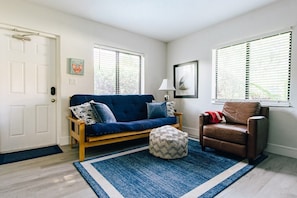 Ein Wohnzimmer mit einem blauen Sofa, einem braunen Ledersessel, einem kleinen Hocker und einem blauen Teppich.