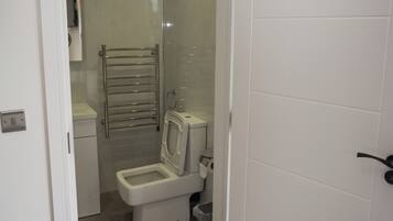 Un baño pequeño y moderno con inodoro, cabina de ducha de vidrio y un perchero para toallas.