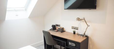 A modern bedroom with a skylight, a desk with a computer, a chair, a bed, and a TV mounted on the wall.